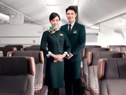 Smiling flight attendants in dark green uniforms stand in the aisle of an EVA Air Premium Economy cabin